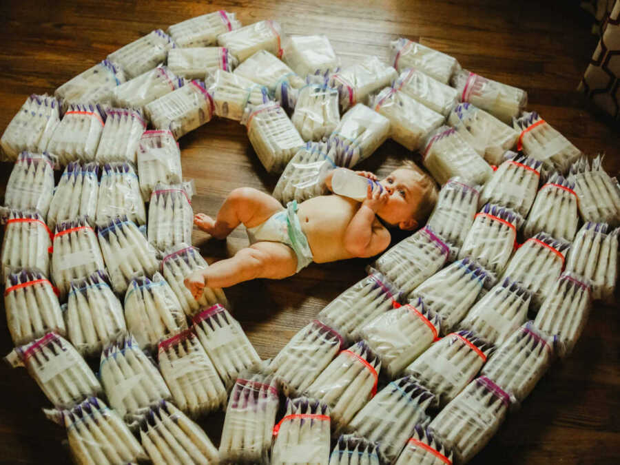 baby laying on floor surrounded by bags of breast milk in a heart shape