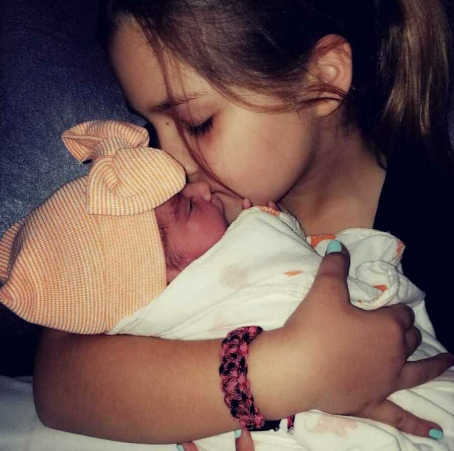 big sister holds her baby sister and gives her a kiss