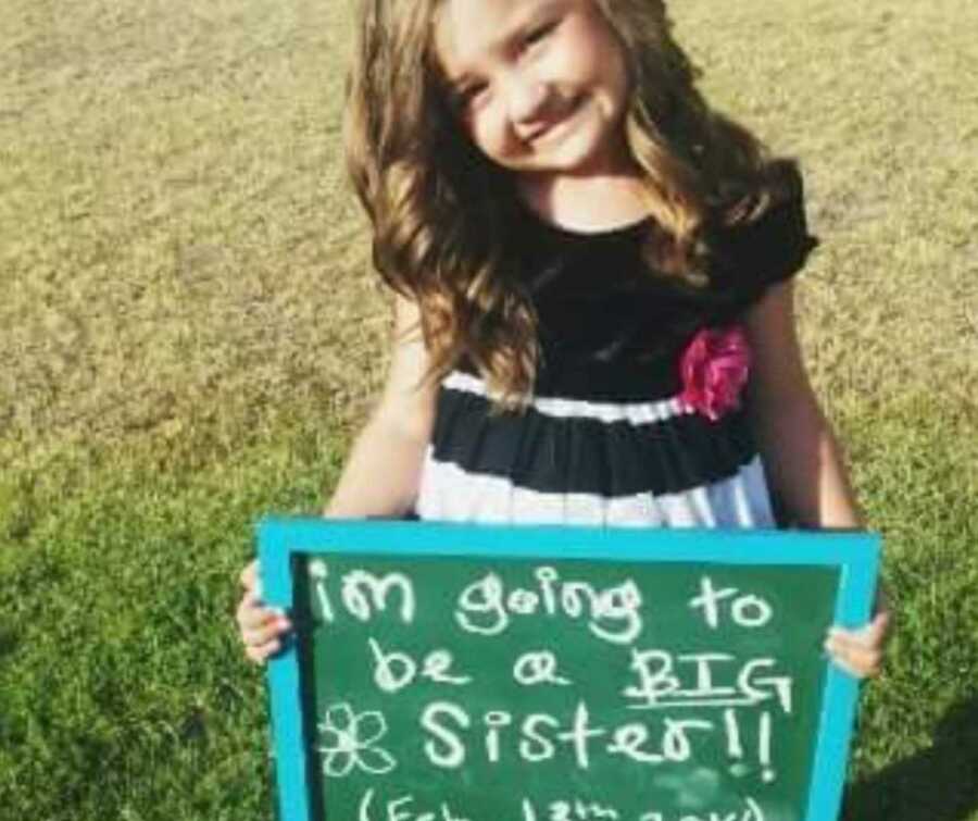 young girl holds up a sign announcing she is going to be a big sister