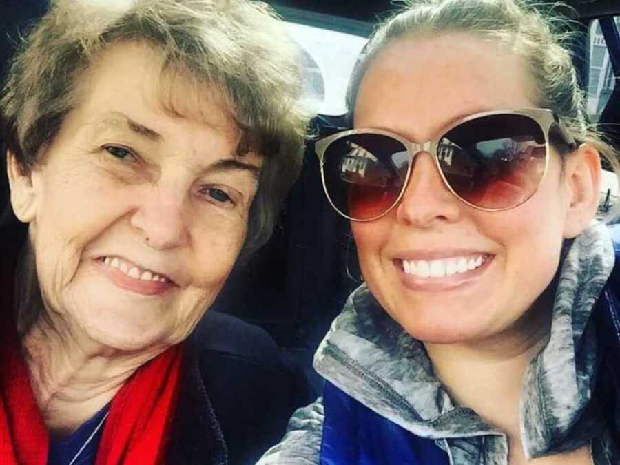 granddaughter wearing sunglasses smiles as she takes selfie with smiling grandmother with alzheimers