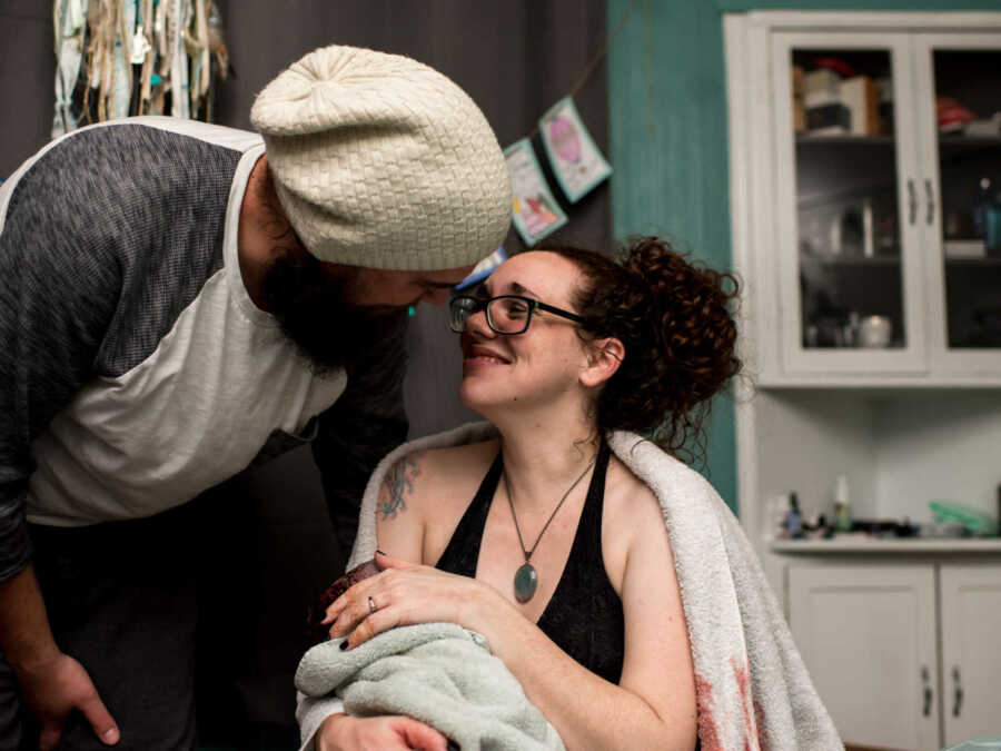 Woman who just gave birth to 11 pound baby wrapped in towel holding newborn looking up at husband