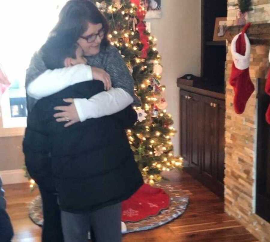 Mom embracing her son in front of the Christmas tree