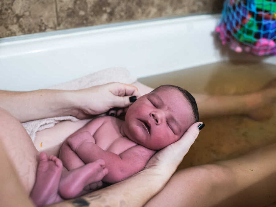 Mother of 11 pound newborn baby holds newborn in lap in bathtub with murky water