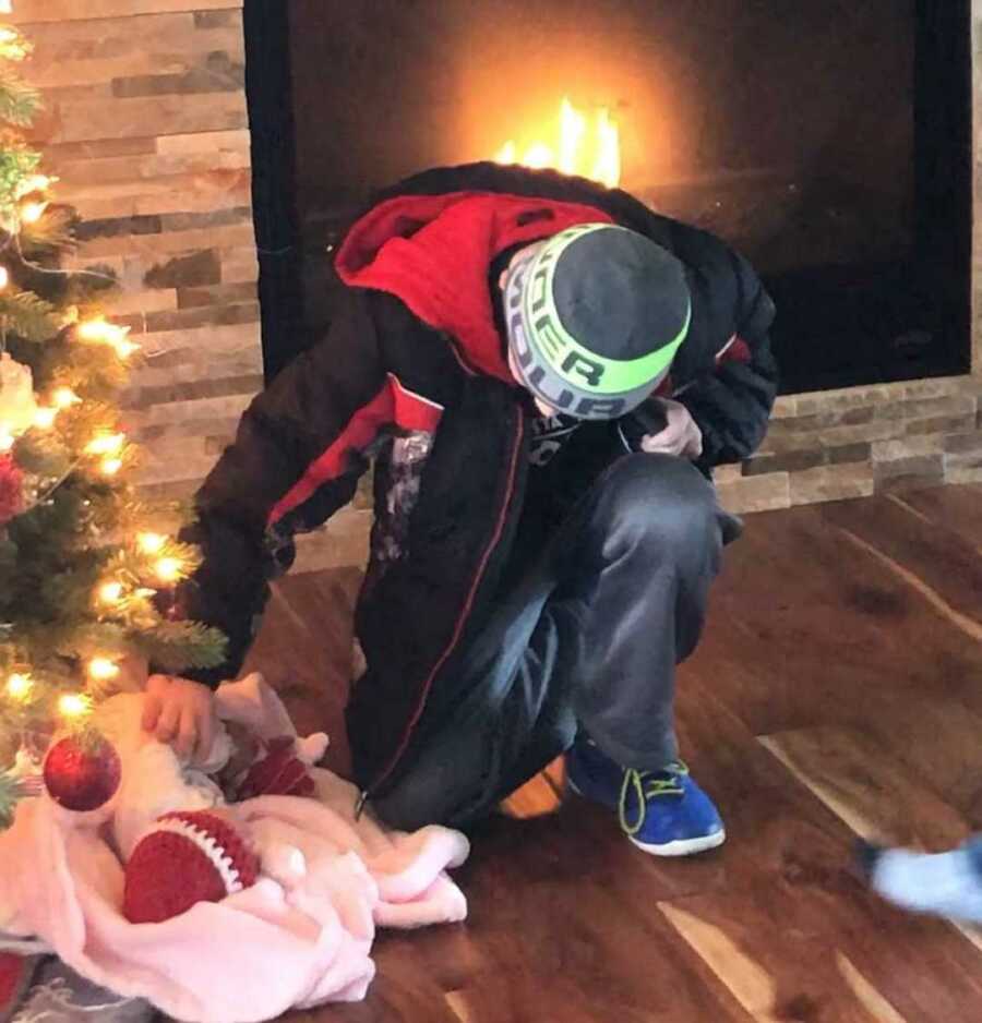 New brother kneeling down to touch newborn sister under the Christmas tree