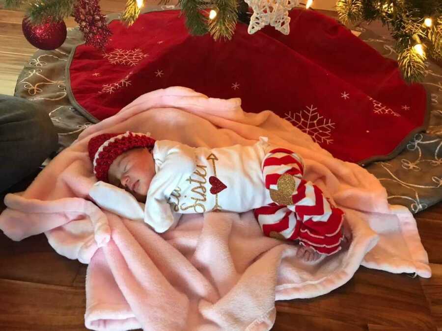 Sleeping newborn baby girl lying under Christmas tree wrapped in a pink blanket 