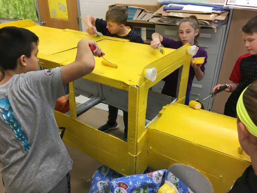 students paint cardboard school bus