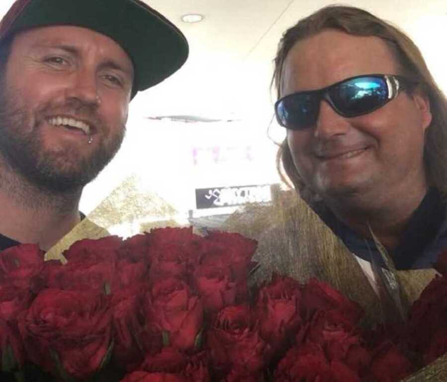 two men smiling holding roses