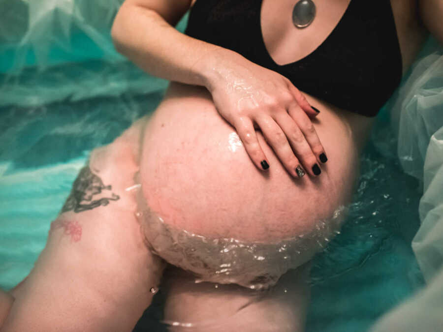 Pregnant woman holding stomach in birthing pool