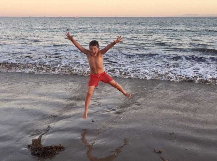 Little boy in red bathing suit jumping above ocean waves