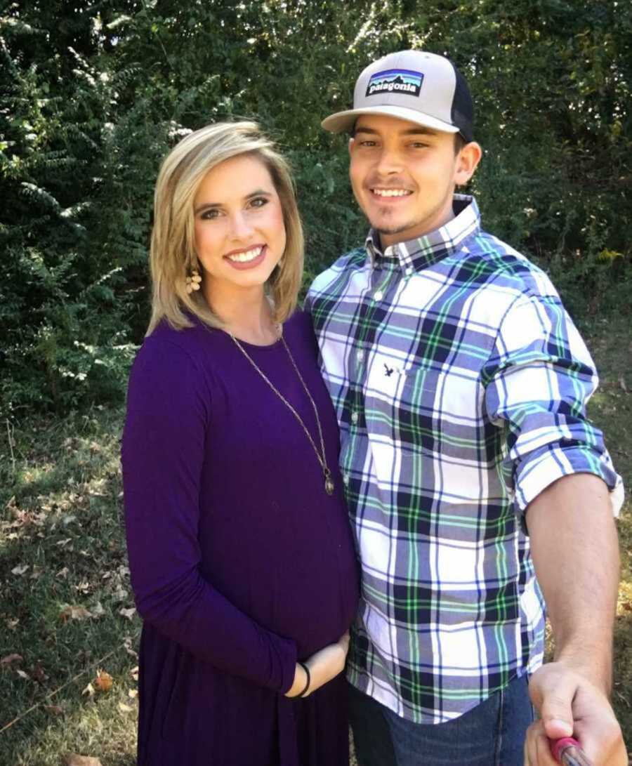 Beaming pregnant woman in purple outfit with husband in a hat and plaid shirt