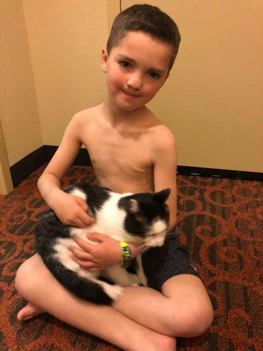 Little boy holding cat while sitting on carpet