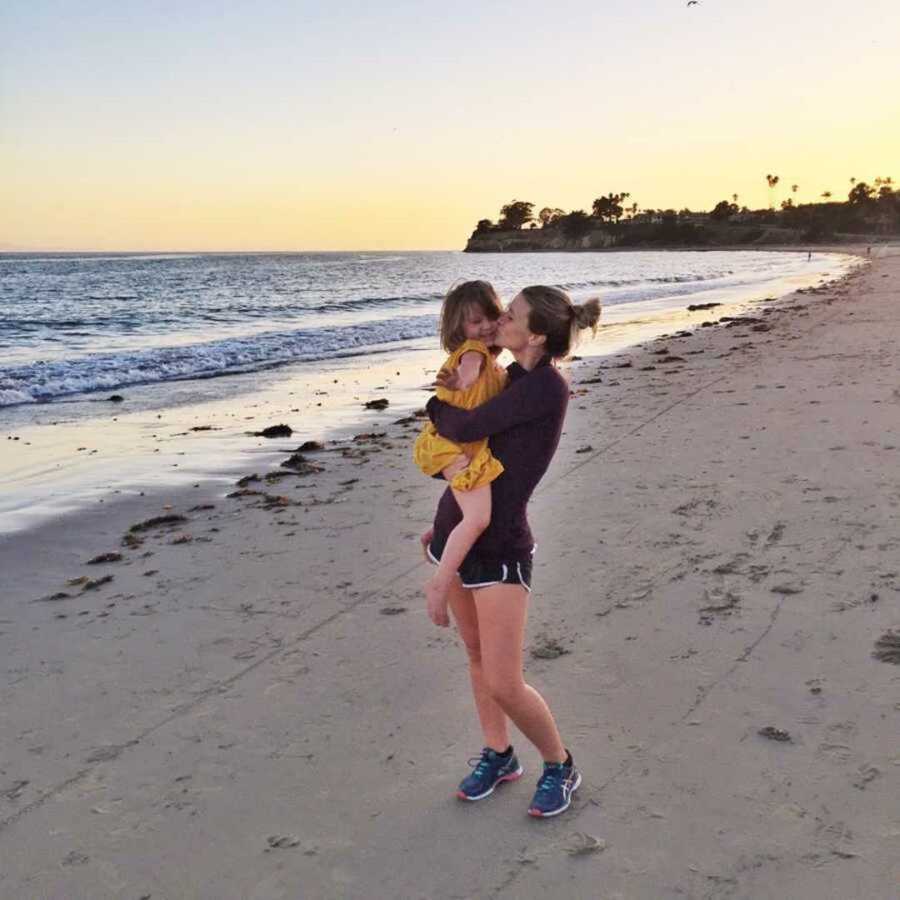 Mom kissing toddler daughter on beach