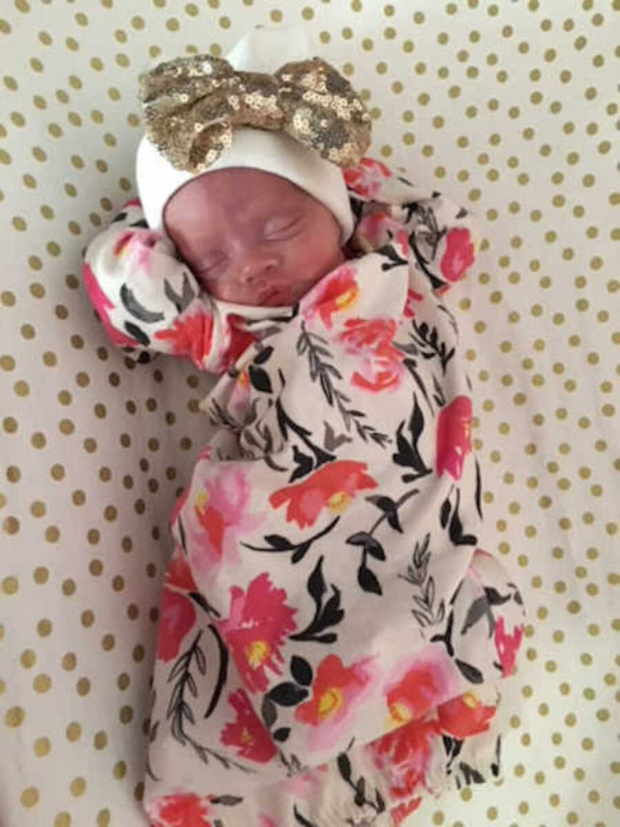 Two pound newborn lying on back sleeping at home with floral outfit on