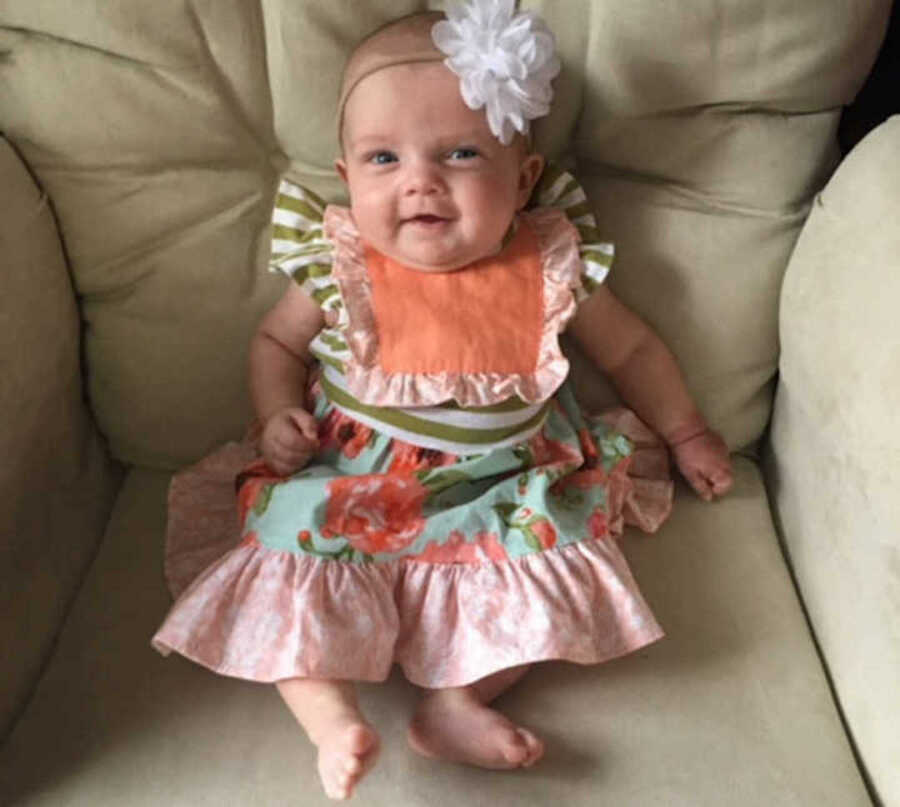 Cheerful baby girl sitting on couch in frilly outfit and headband