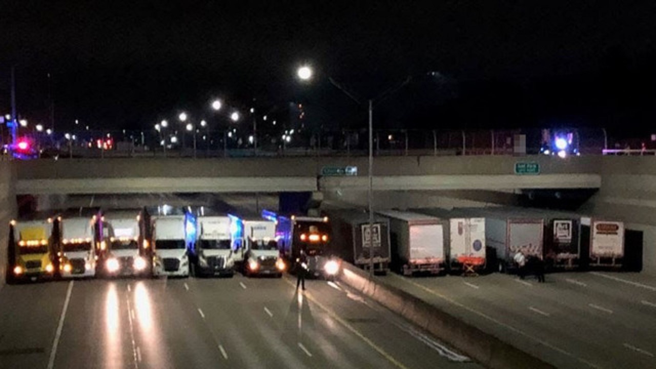 Semi trucks lined up side by side on highway under bridge