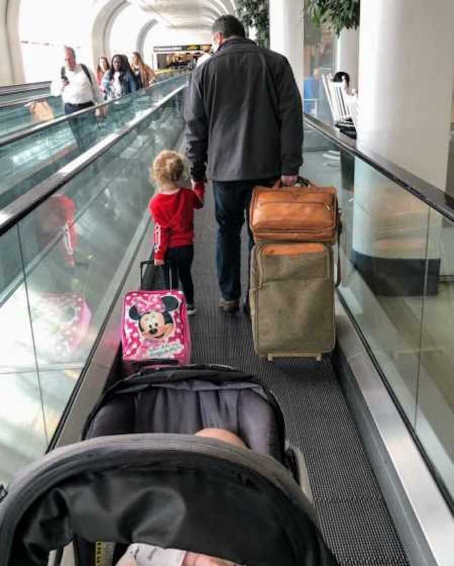 Stranger walking hand in hand with toddler in airport with mother and younger child following