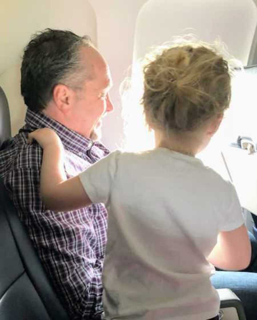 Toddler sits with hand on strangers shoulder on plane who are both looking out window