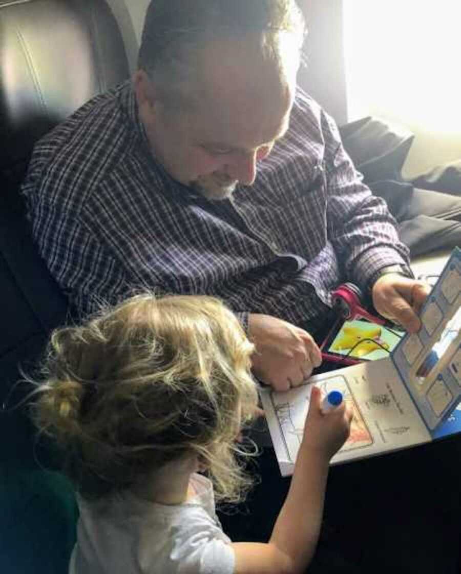 Stranger reading book with toddler whose mother is tending to other child