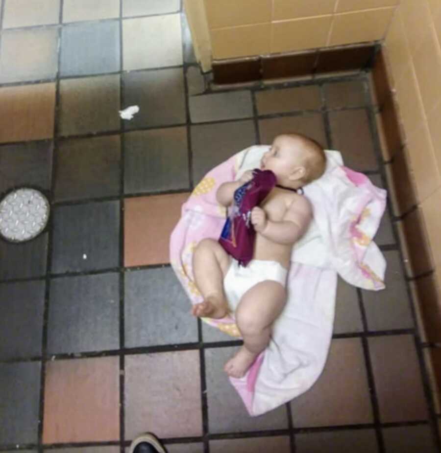 baby girl laid on pink blanket on the floor of a public men's restroom