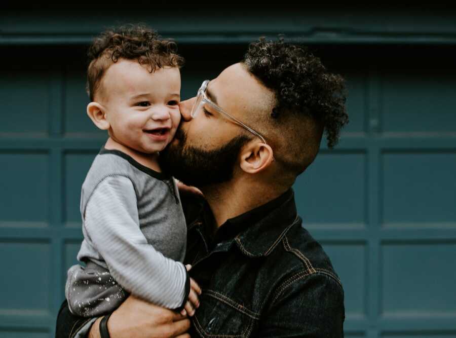 father holds his toddler aged son and gives him a kiss on the cheek
