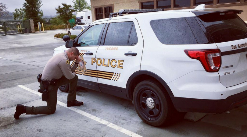 deputy kneeling on the concrete beside his police cruiser praying for the safety of others