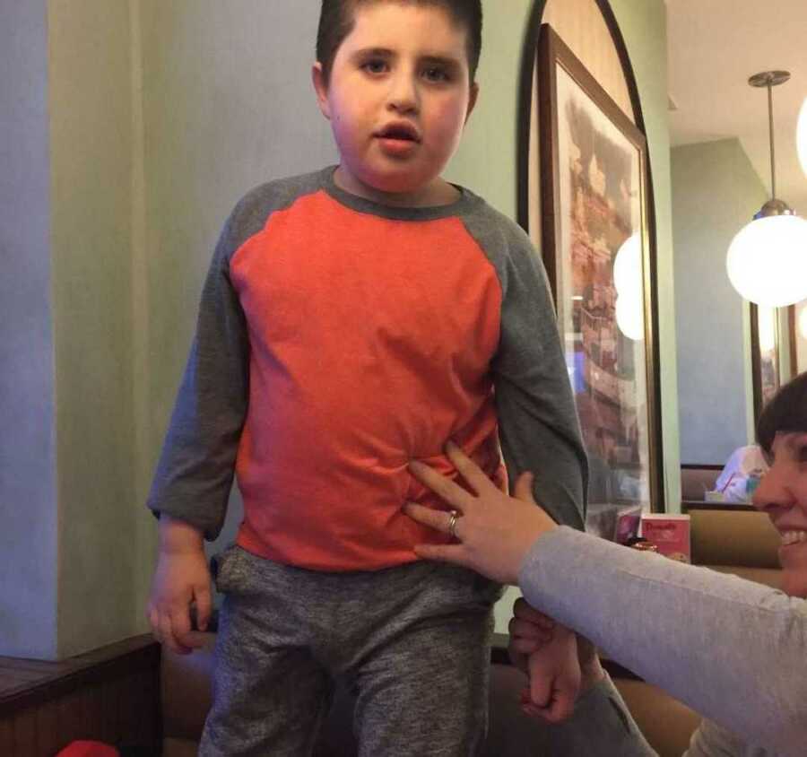 non-verbal autistic boy stands while wearing a grey and orange shirt