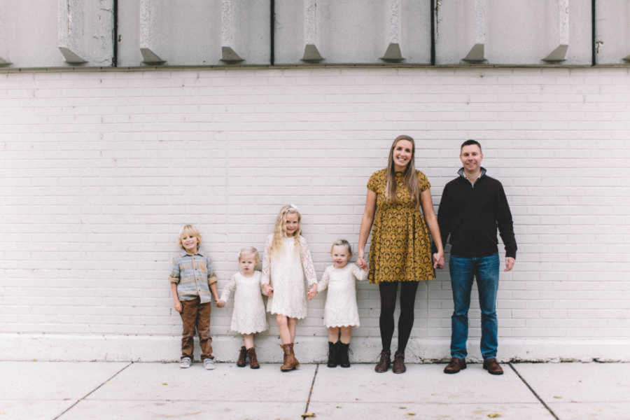 parents holding hands with their 4 children against white brick wall