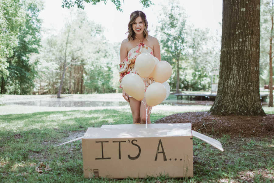 wife stands in front of box saying "it's a" for surprise puppy reveal