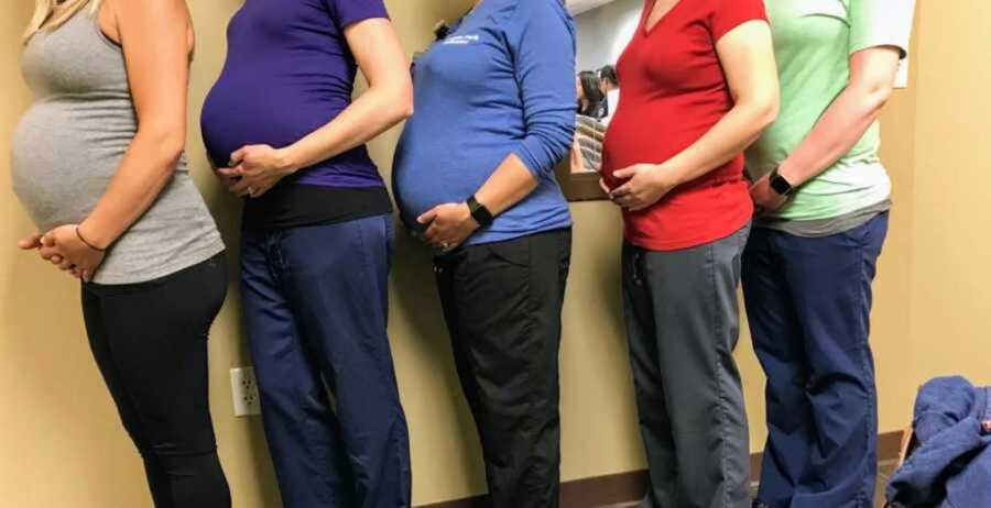 five employees at a pediatric doctors office line up showing off matching belly bumps