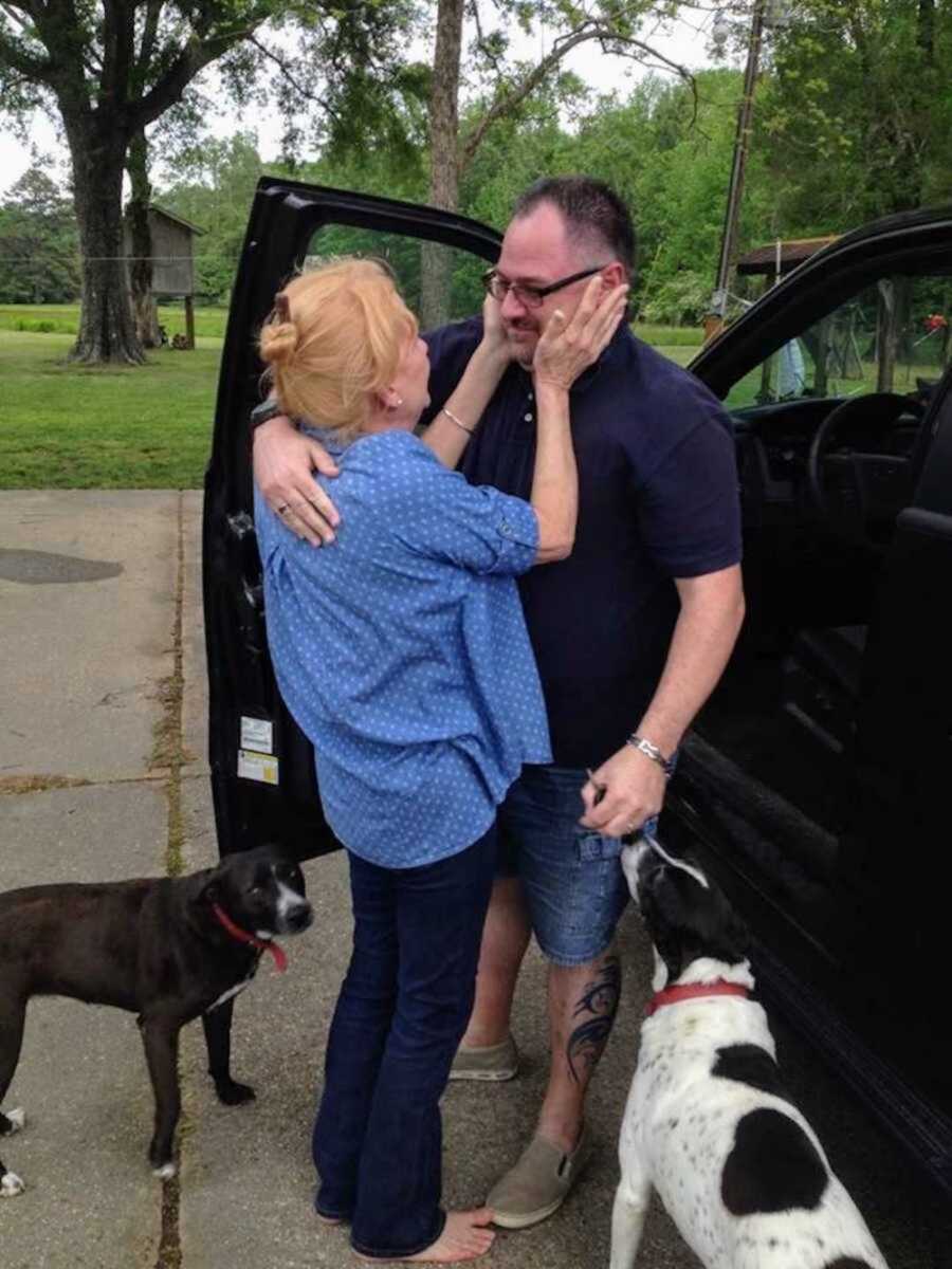 bio mom hugging adult son by car