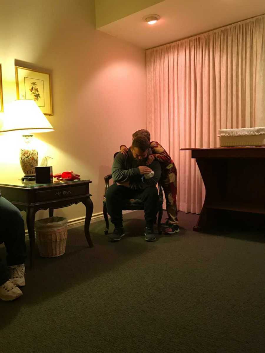 Son embraces dad as they sit in the funeral home