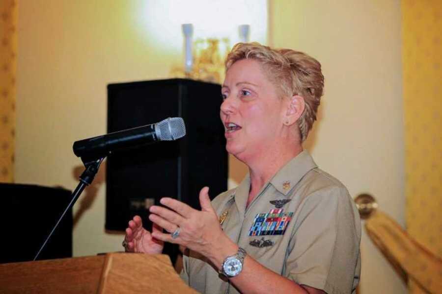 Woman in Navy uniform adorned with medals speaks into a microphone