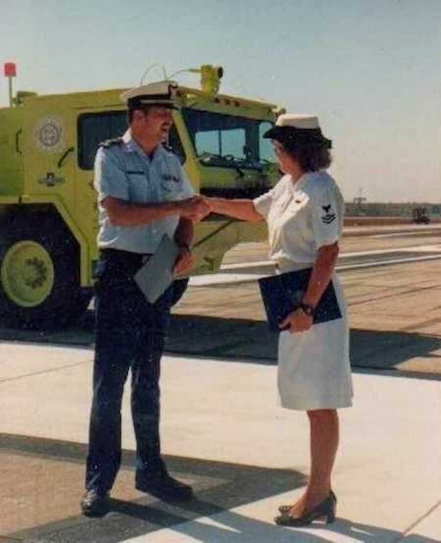 Woman in white Navy uniform shakes a mans hand 