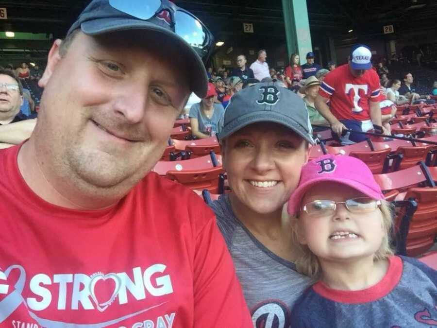 Mom and dad sit with their daughter at a Boston Red Sox game