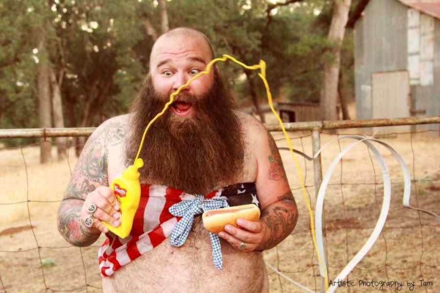 Surprised bearded man holding a hotdog with mustard squirting everywhere