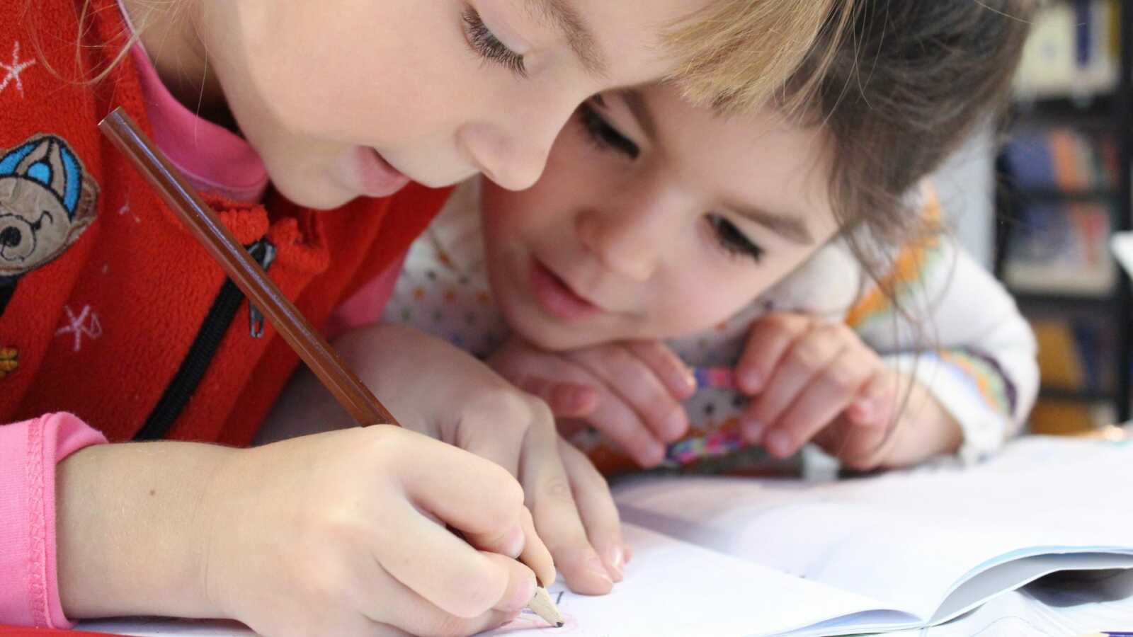 One child writing on a piece of paper and another is closely watching