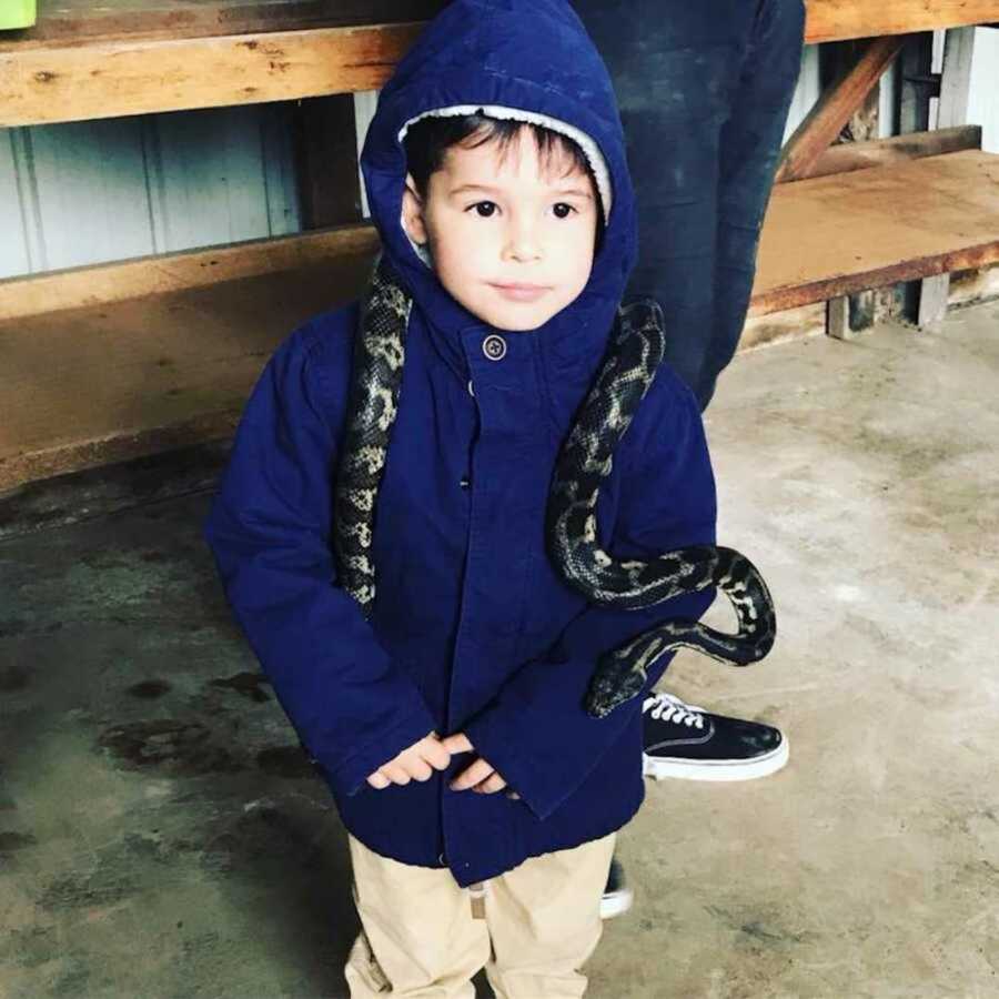 Little boy in blue coat holds a snake on his neck