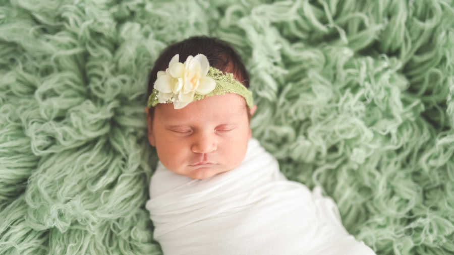 Newborn whose mother died giving birth to her but was brought back to life sleeps in white blanket on green rug