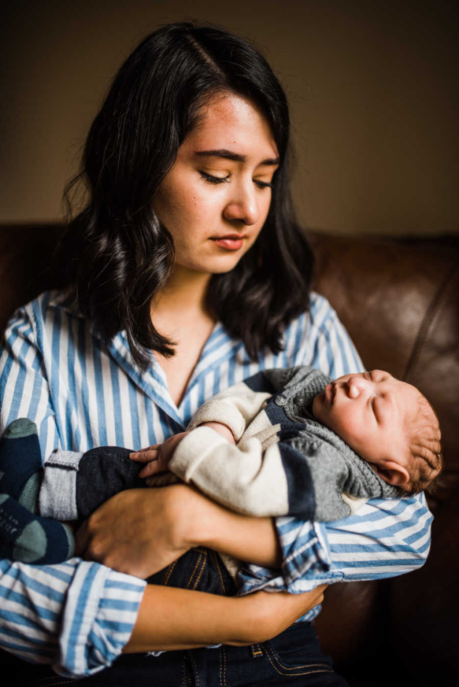 Aunt sadly gazing at newborn nephew in her arms