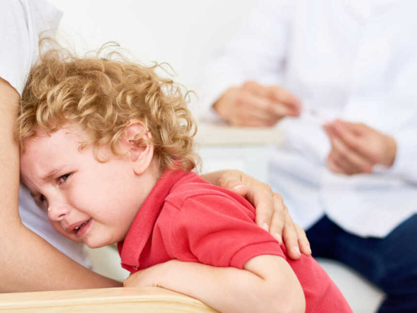 Portrait of crying little boy hugging mother during appointment with doctor
