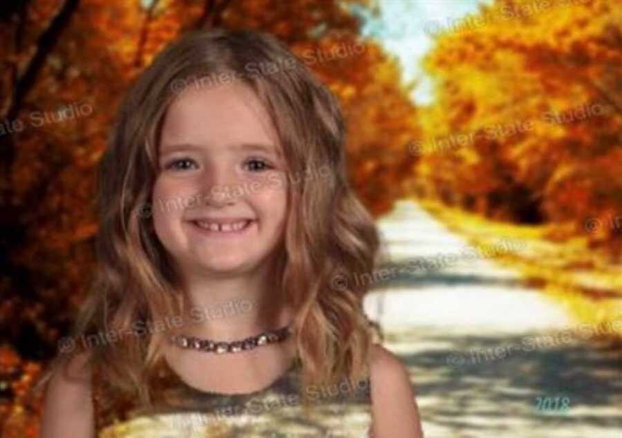 Little girl's head floating on street beside trees wearing green dress that blends in with green screen