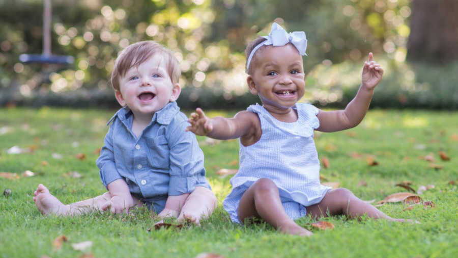 Two infant siblings smiling while sitting on grass