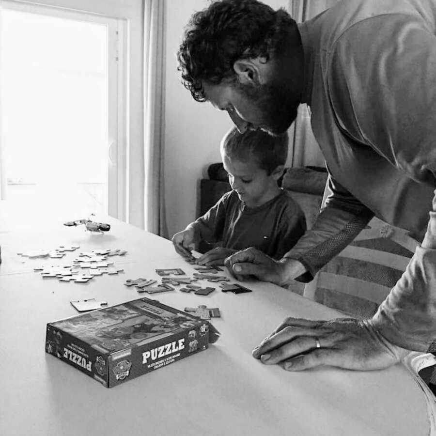 Father standing over table where son is doing a puzzle