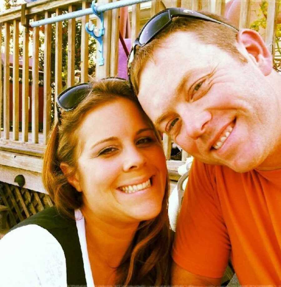 Husband and wife smile in selfie beside wood porch