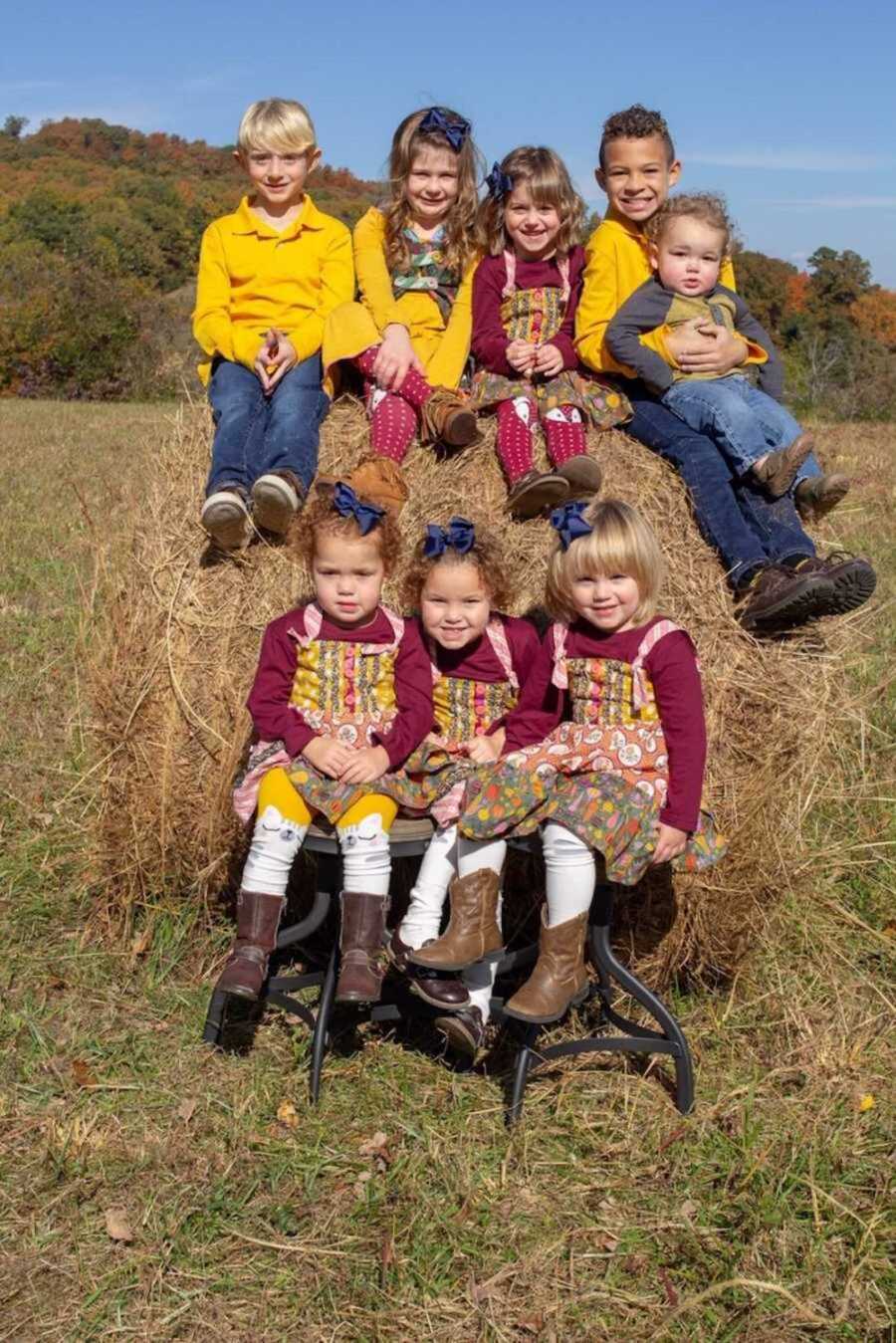 Five foster children sit on top of hay bale while the other three sit on bench below them