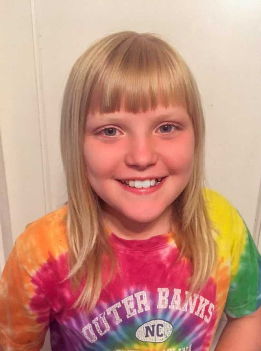 Girl with blonde hair and bangs smiles in tie dye t shirt