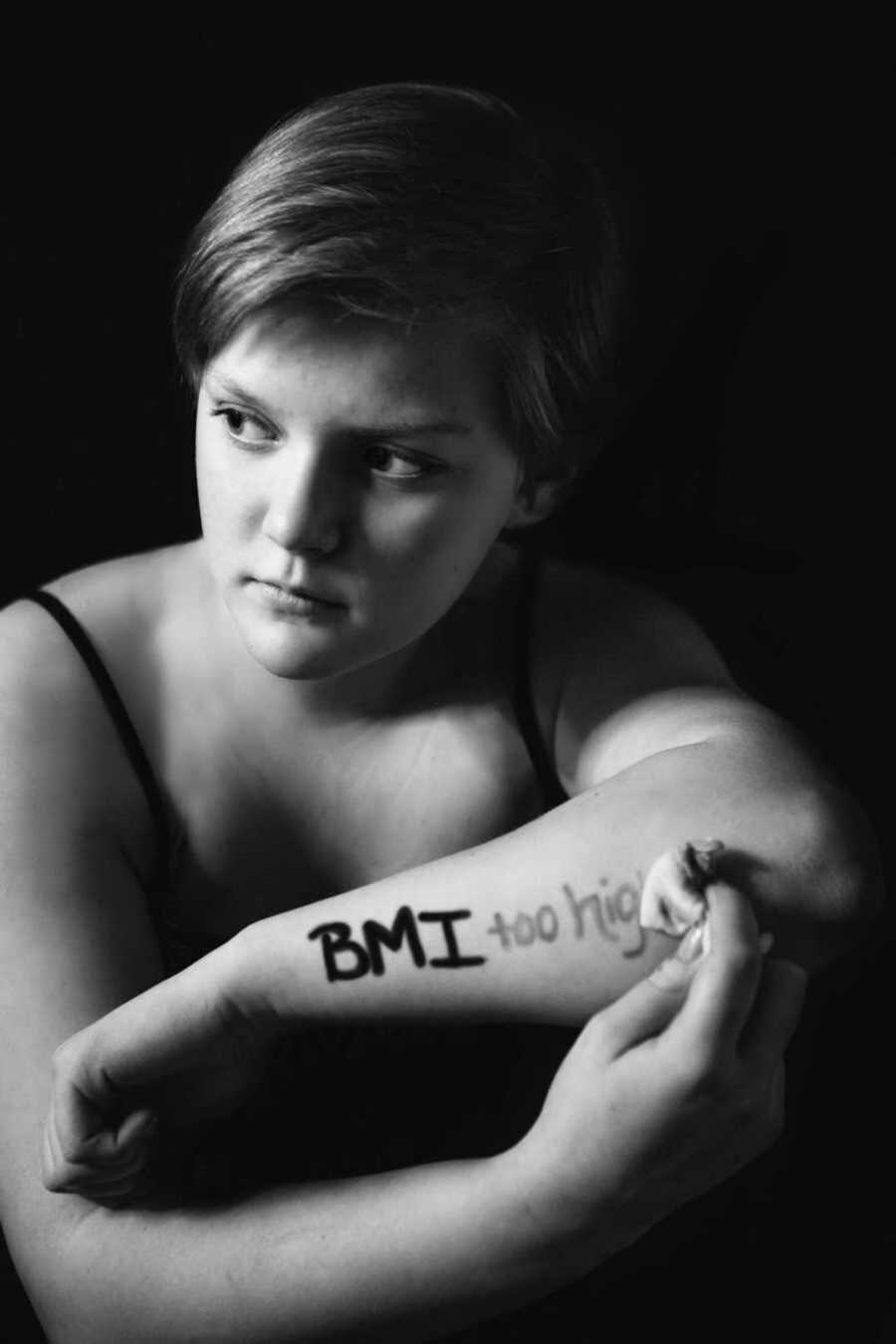 Girl wiping away words "BMI too high" off painted forearm