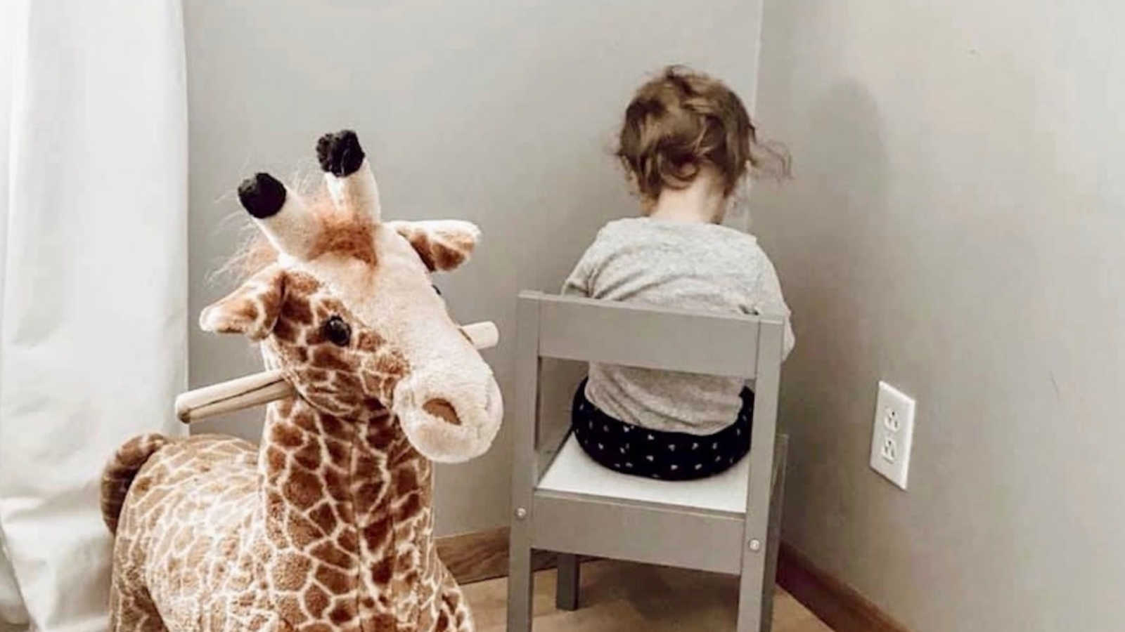 child sitting in timeout next to stuffed giraffe