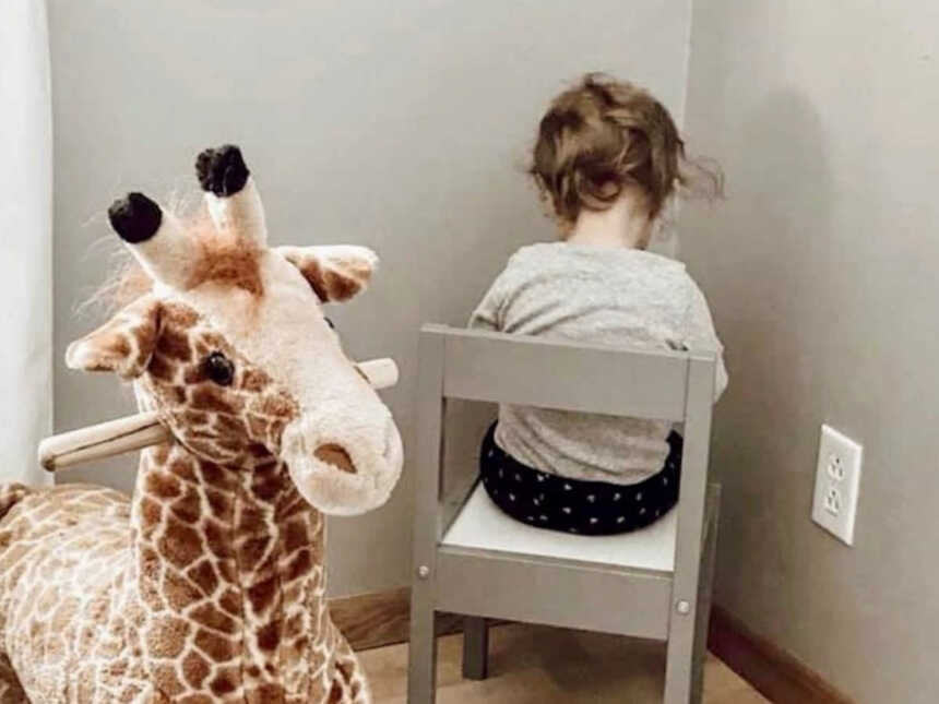 child sitting in timeout next to stuffed giraffe