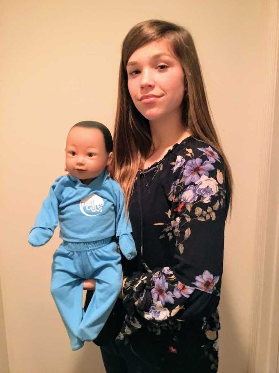 Teen smiling while holding fake baby 